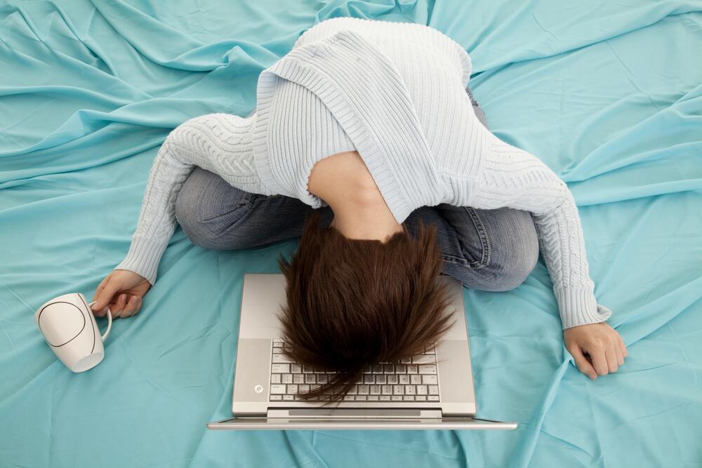 девушка лежит на кровати скрестив ноги и упав лицом в клавиатуру лежащего перед ней ноутбука